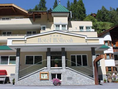 Budynek hotelu z białą elewacją, zielonym dachem i otaczającą naturą w tle