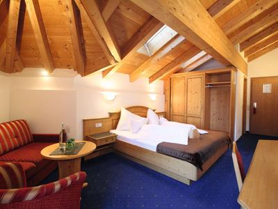 Przytulny pokój hotelowy z drewnianym sufitem, podwójnym łóżkiem, sofą i niebieskim dywanem.