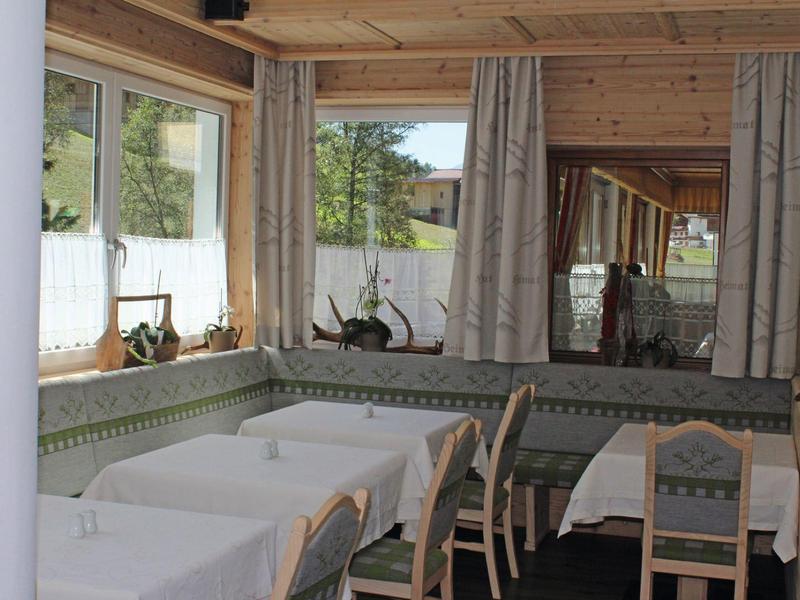 Kuschelige Eckbank mit grünen Polstern und Holztisch in hellem Raum mit großen Fenstern und Gardinen.