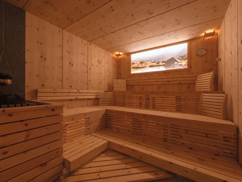 Helle Holzsauna mit mehrstufigen Sitzbänken und beleuchtetem Panoramafenster zeigt Berglandschaft.
