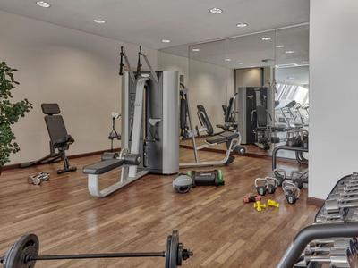 Sala fitness con pavimento in legno, attrezzi per esercizi e pesi in un hotel.