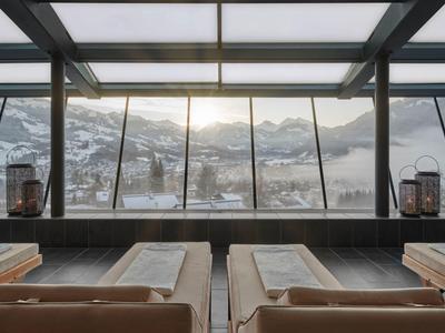 Výhled na zasněžené hory skrz velká skleněná okna z moderního interiéru s pohodlnými lehátky.