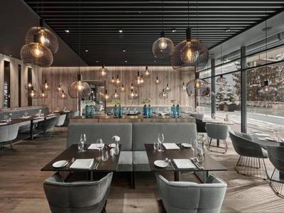 Moderní restaurace s dřevěnou podlahou, šedými židlemi a velkými okny s výhledem na hory.