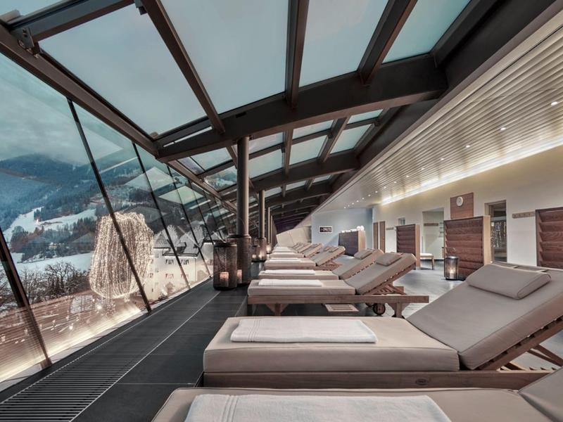 Moderní lounge s lehátky a panoramatickými okny s výhledem na zasněžené hory.