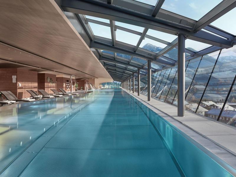 Dlouhý vnitřní bazén s panoramatickými okny a výhledem na hory v moderním hotelu.