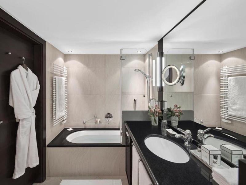 Moderní koupelna s vanou, velkou zrcadlovou stěnou a černou pracovní deskou.