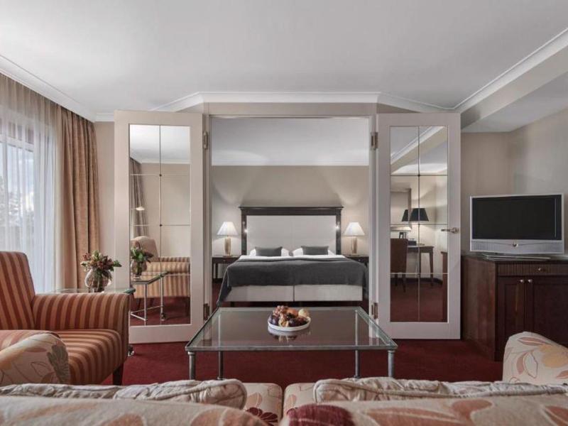 Elegantní hotelový pokoj s nebeskou postelí, křesly, televizí a teplými tóny.