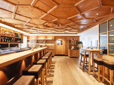 Gemütliche Hotelbar mit Holzdecke, langen Tresen und Barhockern, warm beleuchtet.