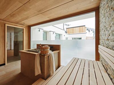 Moderner Saunaraum mit Holzbänken, Steinwand und Glasfenster zum Außenbereich.