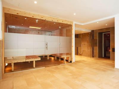 Moderner Wellnessbereich mit Sauna, hellen Fliesen und Holzelementen, klare gläserne Abtrennung.