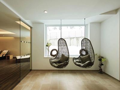 Moderner heller Raum mit großen Fenstern, zwei hängenden Rattanstühlen und hellem Holzboden.