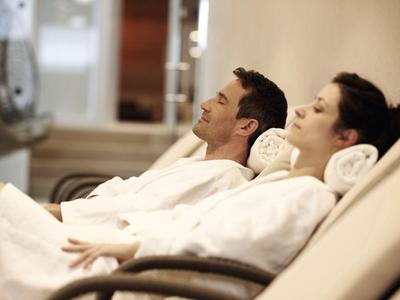 Ein Mann und eine Frau entspannen in Bademänteln auf Liegestühlen in einem Wellnessbereich.