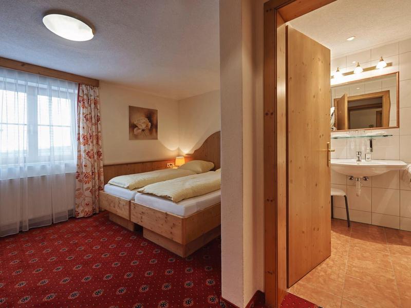 Gemütliches Schlafzimmer mit Doppelbett und angrenzendem hellen Badezimmer mit Waschbecken.