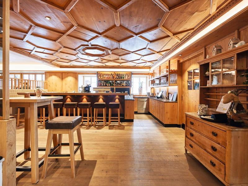 Große, helle Holzbar mit hohem Deckenmuster, Holzstühlen und reich bestückten Regalen.