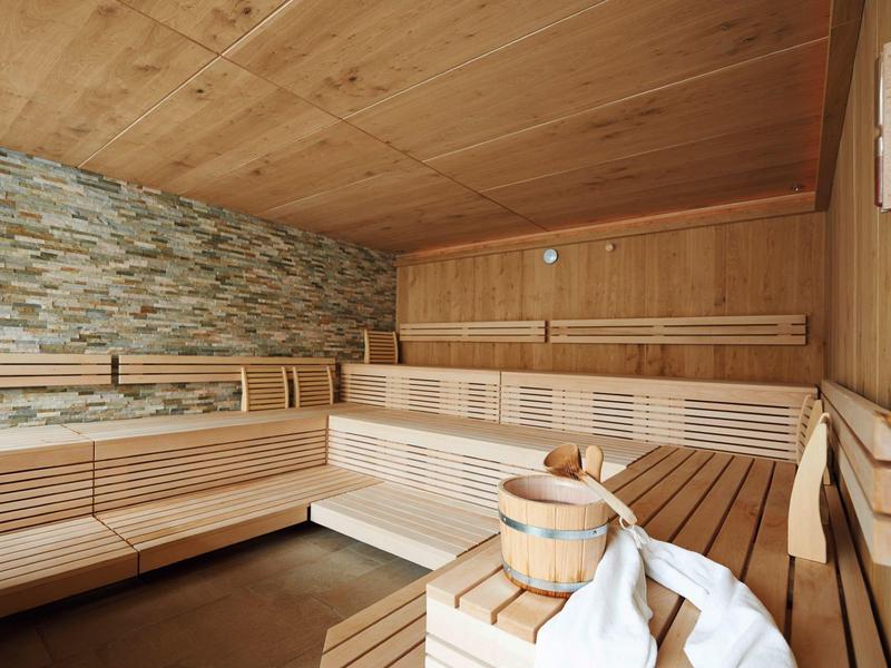 Moderne Sauna mit Holzvertäfelung, Steinwand und Holzbänken in warmem Licht.