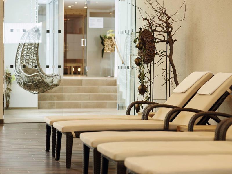 Hell eingerichteter Ruheraum mit beigen Liegen, Holzboden und Glaswand zur Treppe im Hintergrund.