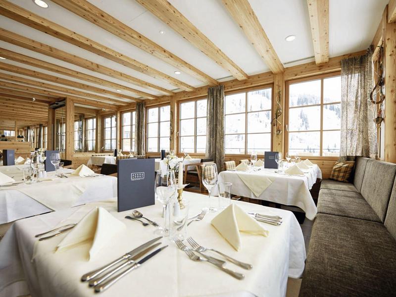 Helles Restaurant mit Holzbalken, großen Fenstern und weiß gedeckten Tischen mit Besteck.