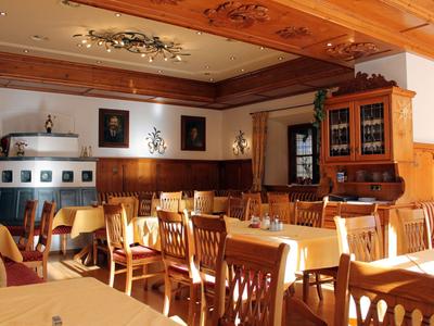 Helles, rustikales Restaurant mit Holztischen, Stühlen und dekorativer Kachelofenanlage.