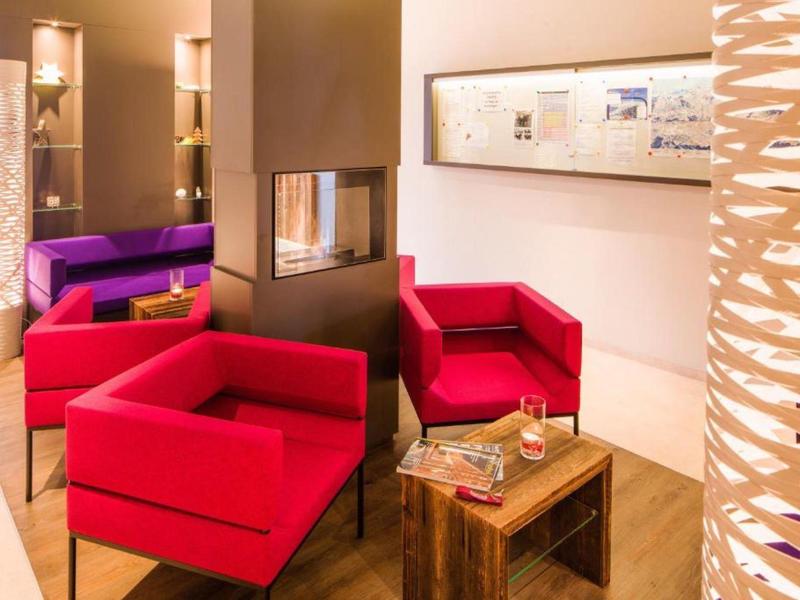 Coin salon confortable avec fauteuils rouges, cheminée et table en bois dans une ambiance chaleureuse.