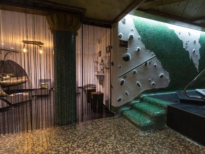 Innenraum mit grüner Treppe, grünem Teppich und einer Wand mit Löchern sowie Retro-Möbeln.