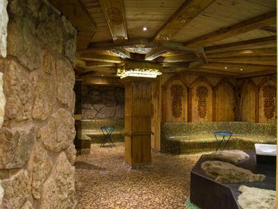 Rustikaler Raum mit Steinwänden, Holzbalken, gepolsterten Sitzflächen und Teppichboden.