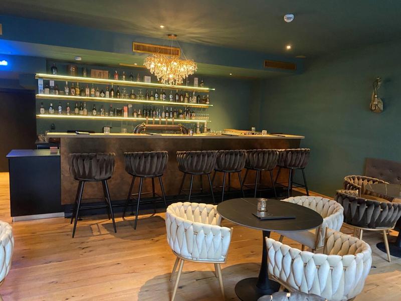 Modernes Café mit schwarzer Bar, goldenen Hockern und gemütlichen weißen Sesseln an runden Tischen.