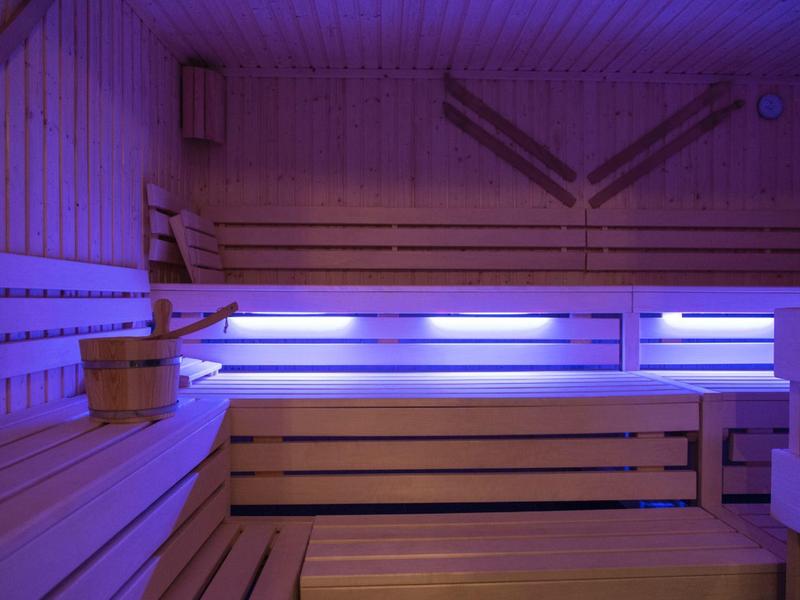 Moderne Sauna mit Holzbänken und violettem LED-Licht an den Wänden.