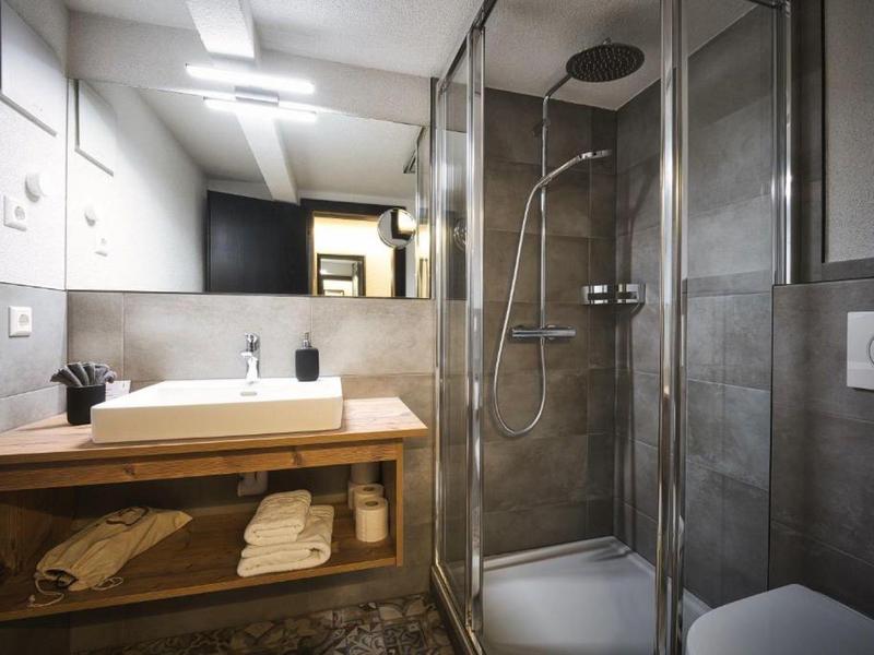 Modernes Badezimmer mit Dusche, Waschbecken auf Holzablage und grauen Wandfliesen.