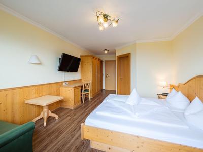 Habitación de hotel luminosa con cama doble, muebles de madera, TV y mesa pequeña con silla.