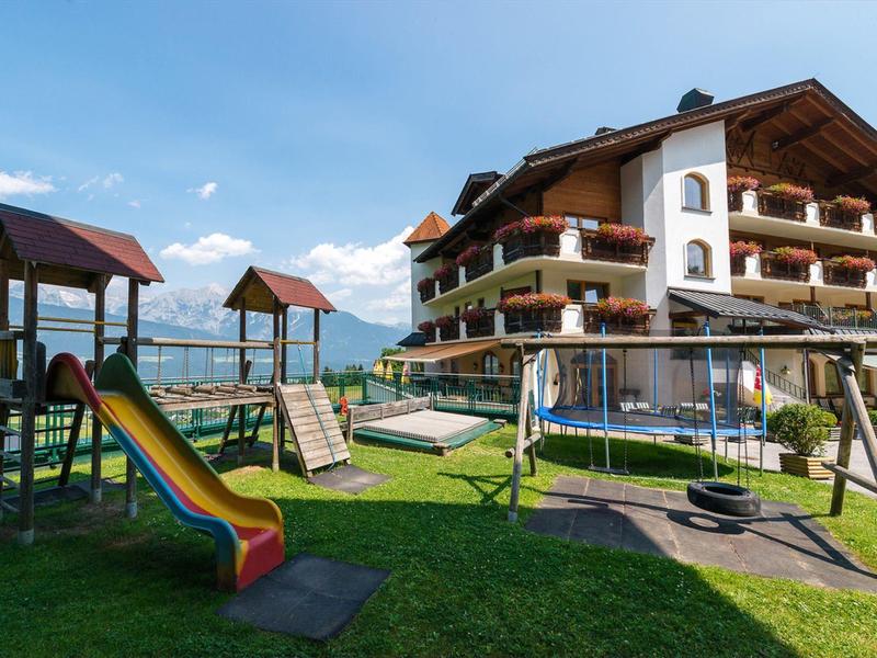 Dětské hřiště s klouzačkou a houpačkami před hotelem v horách.
