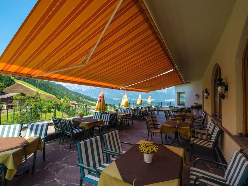 Příjemná terasa s stolem, židlemi a oranžovým pruhovaným slunečníkem s výhledem na zelené hory.