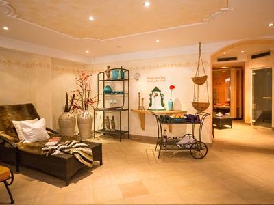 Pohodlná místnost s koženým lehátkem, dekorativními rostlinami a teplým osvětlením v pozadí.