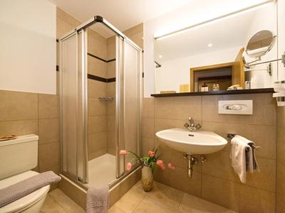 Malá hotelová koupelna se sprchou, umyvadlem, toaletou a světlými dlaždicemi.