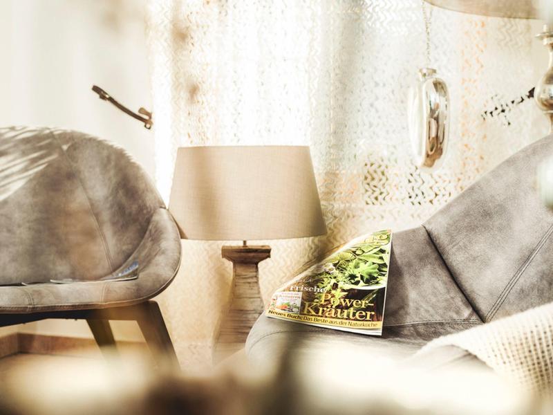 Světelné místnosti s dvěma šedými křesly, stolkem s lampou a knihou před bílými závěsy.