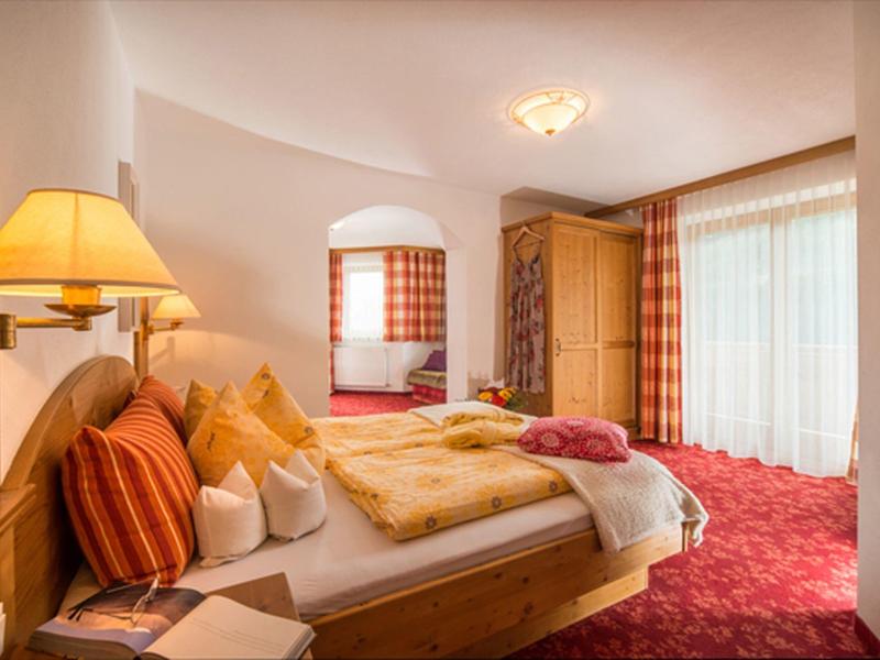 Pohodlný hotelový pokoj s dřevěným nábytkem, teplými barvami a červeným kobercem.