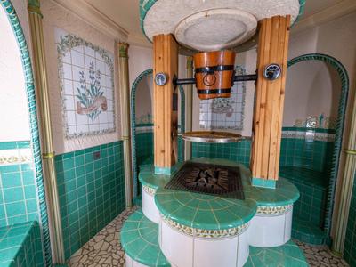 Fontana interna rotonda con piastrelle verdi e bianche e colonne di legno in un bagno.