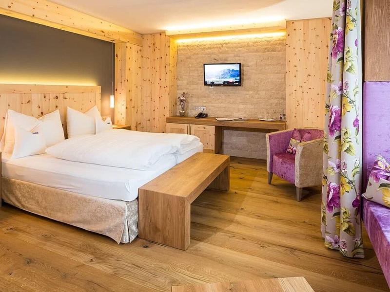 Camera d'hotel moderna con letto matrimoniale, pavimento in legno e area salotto accogliente con accenti viola.