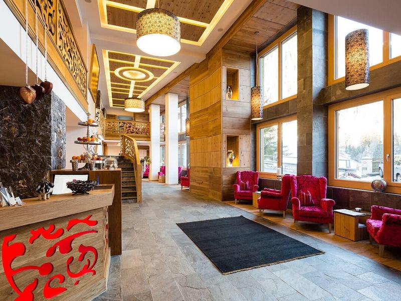 Hall d'hotel luminoso con pannellature in legno, poltrone rosse e grandi finestre