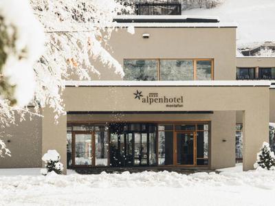 Modernes Alpenhotel mit hellem Putz, großen Fenstern und verschneiter Umgebung im Winter.