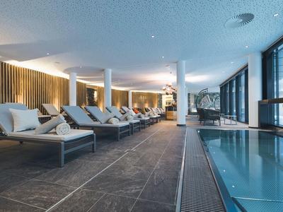 Moderner Wellnessbereich mit Pool, Liegestühlen und großen Fenstern für Tageslicht.