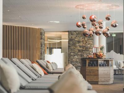 Helle Lounge mit gemütlichen grauen Sofas, hängender Lampe mit kupfernen Kugeln und Steinwand im Hintergrund.