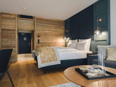 Modernes Schlafzimmer mit Holzakzenten, großem Bett, schwarzen Stühlen und runden Holztisch.