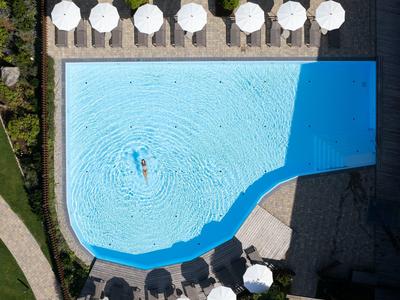 Rechteckiger Pool mit blassem blauen Wasser, umgeben von weißen Sonnenschirmen und Liegestühlen.