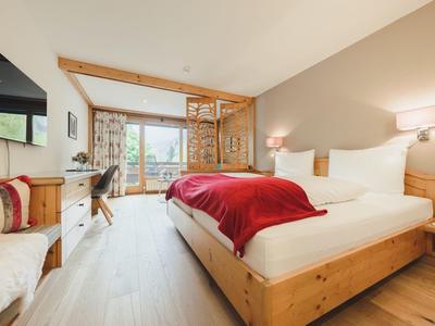 Helles Schlafzimmer mit Holzmöbeln, großem Bett, roter Decke und Fenster mit Blick nach draußen.