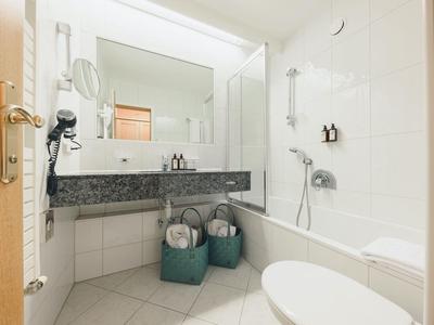 Helles Badezimmer mit weiß gekachelten Wänden, Badewanne, großem Spiegel und Waschbecken aus dunklem Marmor.