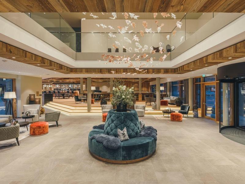 Moderne, helle Hotellobby mit zentralem blauen Sofa, Holzdecke und großen Fenstern.