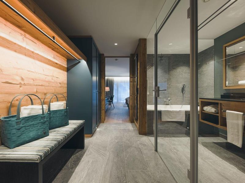 Moderner Flur mit Holzwand, Bank, blauem Korb und angrenzendem Bad mit Glaswand und Waschtisch.