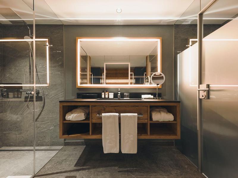 Moderne Badezimmereinrichtung mit großem Spiegel, hängendem Waschbecken und abgetrennten Glasduschen.