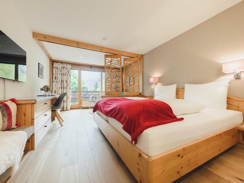 Helles Schlafzimmer mit Holzmöbeln, großem Bett, roter Decke und Fenster mit Blick nach draußen.