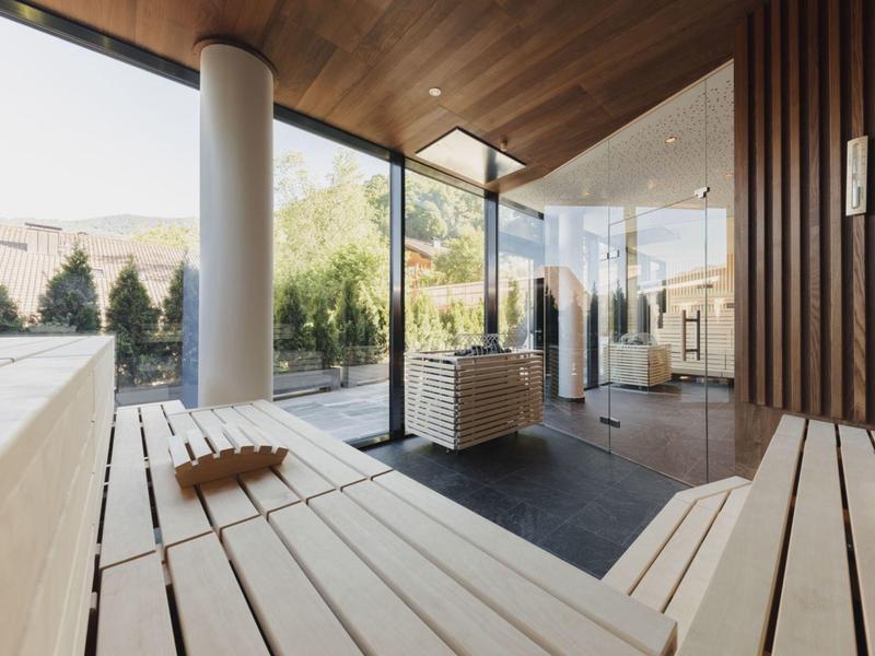Moderner Saunaraum mit hellen Holzbänken, großen Glasfenstern und Blick auf Außenbereich.